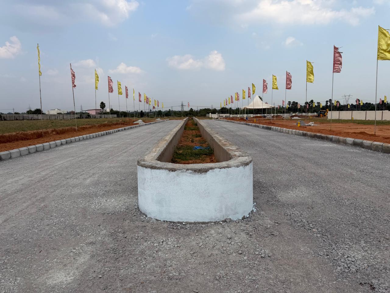 Main avenue at Eastern Meadows with a whitewashed, rounded-end landscaped median running down the centre of a compacted metal road, kerb stones on both edges and flags lining the route