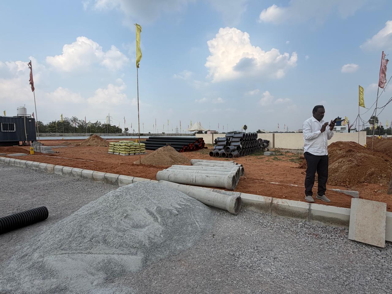 Pipe and material staging area at Eastern Meadows: stacks of black HDPE pipes, precast concrete pipes, cement bags and aggregate beside a kerbed road