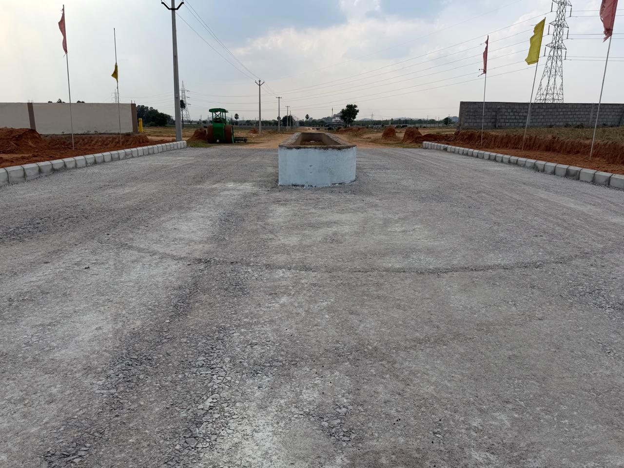 Second stretch of the median road at Eastern Meadows, with the whitewashed median, kerbed edges, overhead power lines along the road and a road roller parked ahead