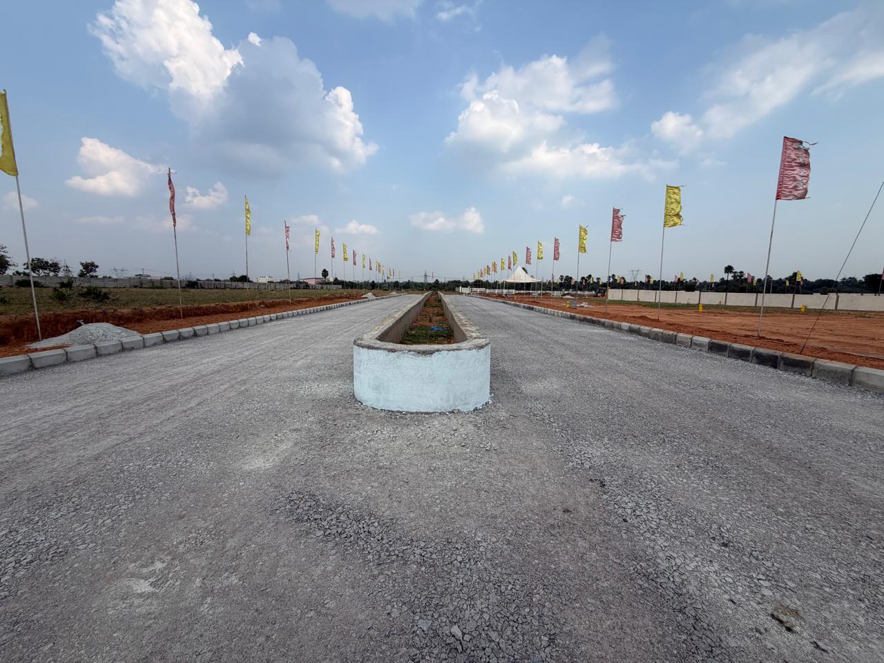 Wide-angle view down the Eastern Meadows main avenue, with the planted central median, metalled carriageways and kerbed road edges stretching to the horizon under a blue sky