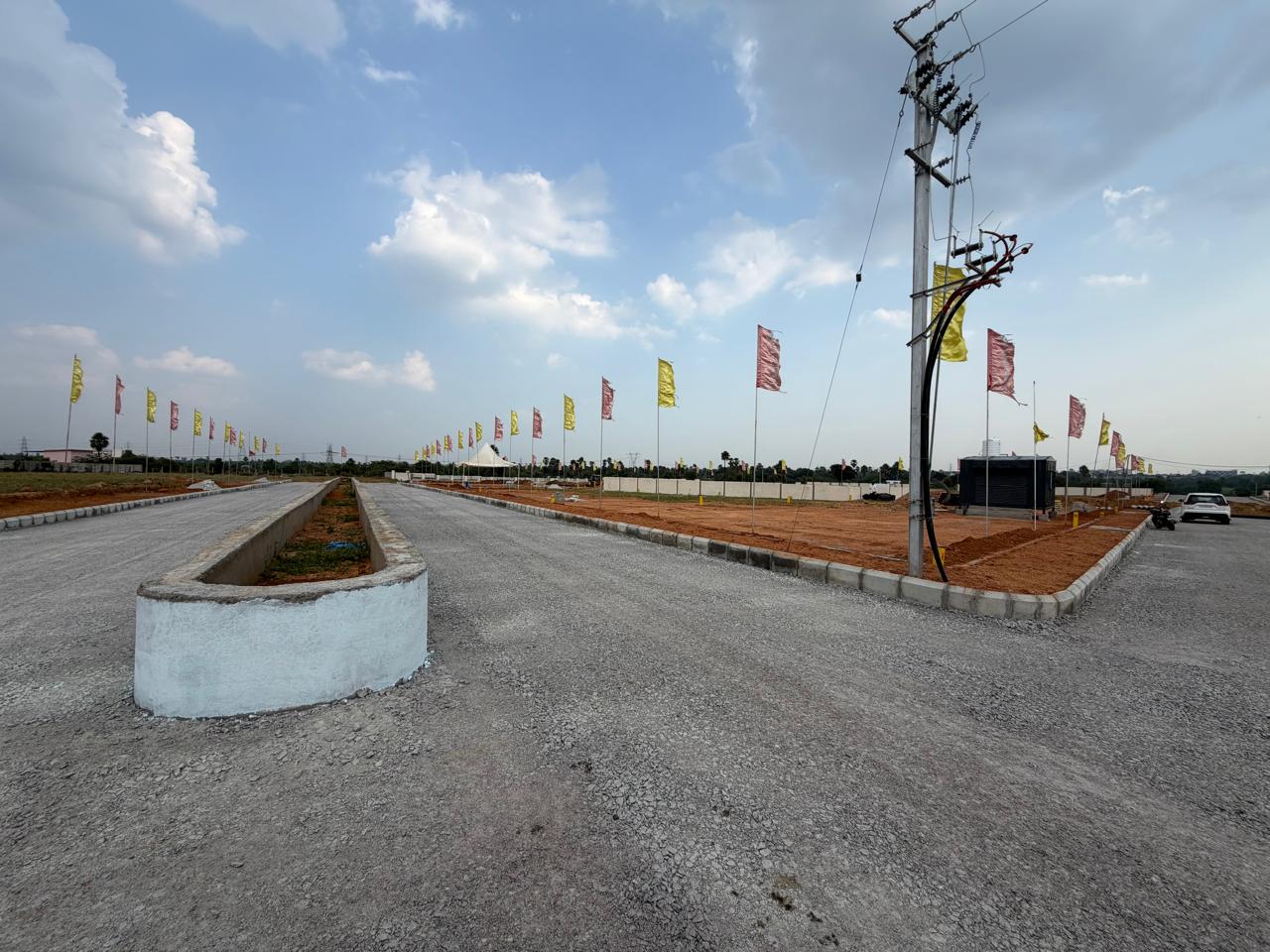Road junction at Eastern Meadows where the median avenue meets a cross road, with a kerbed corner plot and an electric pole fitted with insulators and cable drops