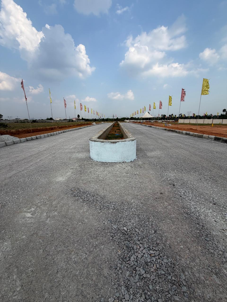 Portrait view along the Eastern Meadows main avenue showing the whitewashed end of the central median and the compacted stone base course in the foreground