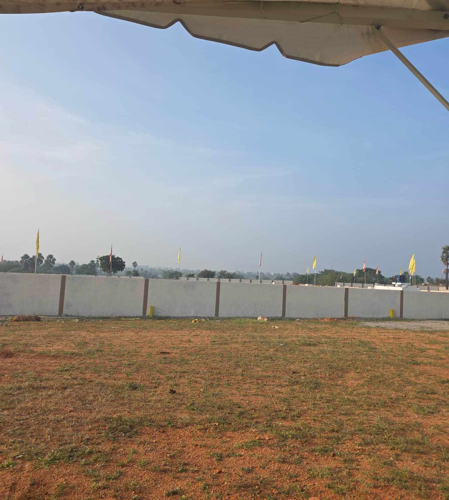 Early-morning view of levelled plot land at Eastern Meadows, with the precast compound wall and boundary flags along the far edge
