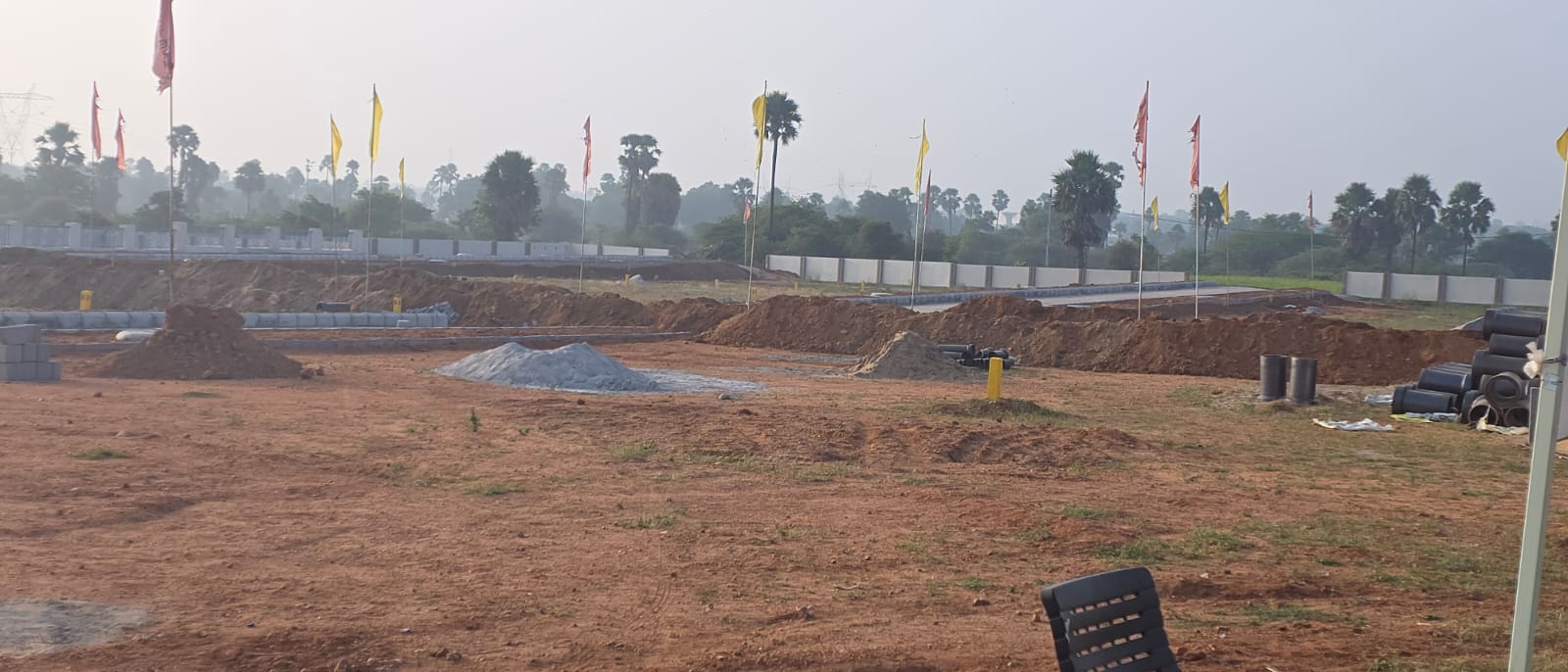 Wide morning view across the Eastern Meadows layout showing aggregate heaps, earthwork along the roads and the flagged boundary